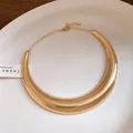 Dettaglio di un girocollo in metallo dorato lucido a forma di mezzaluna su un piatto bianco - Oro