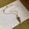 Dettaglio ravvicinato di un ciondolo a forma di pesce dorato con smalto nero su base. - Collana-Oro-Nero
