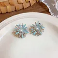 Close-up of zircon enamel firework stud earrings with a pearl center on a white plate. - Fireworks Style (HE32747) / Silver-Blue