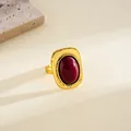 Detalle de un anillo retro dorado con una piedra ovalada de color rojo oscuro elegante - Estilo Ovalado (HR3616) / Oro Antiguo-Rojo