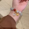 Elegant beaded cat-eye stone bracelet with red and yellow charms worn on female wrist - White