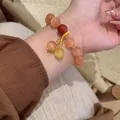 Elegant cat's eye stone beaded bracelet with red and yellow accent charm worn on person's wrist - Orange