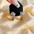 Close-up of elegant white enamel flower earrings with rhinestone leaf drop detail. - Gold Flower Leaf Stud Earrings