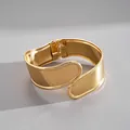 Close-up view of a wide gold-tone geometric bangle with hinge closure and smooth finish. - Open Geometric Bangle