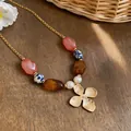 Primer plano de collar de vacaciones con cuentas de cerámica y colgante flor dorada. - Collar-Rosa-Azul-Café (HN12250) / Multicolor