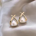 Close-up detail of minimalist gold-plated cross earrings with heart-shaped cream pearls - Gold