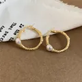 Dettaglio di orecchini vintage dorati con texture stropicciata e accenti di perle - Oro