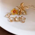 Vista macro dettagliata di eleganti anelli dorati con fiori 3D su sfondo minimalista - Fiore 3D / Oro-Giallo