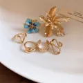 Primo piano di eleganti anelli aperti dorati a fiore e onde su una superficie in ceramica. - Fiore 3D / Oro-Blu
