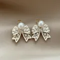 Close-up of French vintage hollowed-out bow stud earrings with pearls and crystal - Hollowed Bow Style (HE34170) / Silver and White