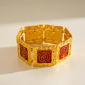 Vista macro di un bracciale vintage dorato con inserti in smalto rosso e spirali - Oro-Rosso