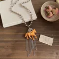 Detail view of a playful orange resin horse pendant with silver tassel on a bead chain - Pony Pendant Tassel Style / Silver-Coffee