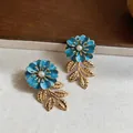Detaillierte Ansicht eleganter blauer Emaille-Blumenohrringe mit Goldblättern und Perlen. - Blau