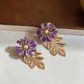 Detaillierte Makroaufnahme eleganter lila Emaille-Blumenohrringe mit goldenen Blättern und Perlen - Lila