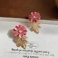 Elegante Detailaufnahme von rosa Emaille-Blumenohrringen mit goldenen Blättern und Perlen - Rosa