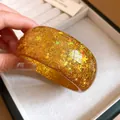 Detailed macro shot of a golden resin bangle with embedded star and snowflake glitter - Brown