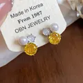 Close-up detail showing exquisite yellow flower zircon and white pearl stud earrings on card. - Yellow