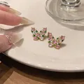 Detail view of butterfly stud earrings with pink and green zircons on a cream plate. - Gold (Pink and Green Inlay)