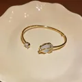 Detailed shot of an elegant gold tulip bangle featuring cat's eye stone and zirconia crystals - Gold