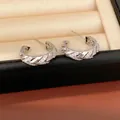 Close-up of silver-plated C-shaped hoop earrings with sparkling zircon stones in a box. - Silver