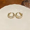 Detail of 14k gold-plated hoop earrings with sparkling zircon on a ceramic plate. - Round Hoop / Gold