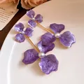Makro-Detailansicht von lila Emaille-Blumenohrringen mit weißen Perlen und Goldfinish - Stahlnadel-Stil / Lila