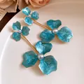 Detailansicht der blauen Emaille-Blumenohrringe mit Perle auf einem weißen Keramikteller. - Stahlnadel-Stil / Blau