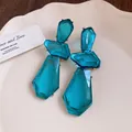 Dettaglio degli orecchini pendenti in resina blu con forme geometriche e castoni dorati. - Blu