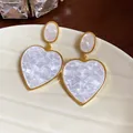 Close-up detail of elegant white resin heart earrings with gold trim and mosaic texture - Gold Heart / White