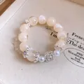 Primo piano di un bracciale romantico con perle crema e un cristallo quadrato fine. - Argento-Bianco