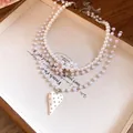 Close-up detail of a pearl beaded necklace with floral accents and heart pendant - White