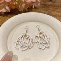 Macro view of white shell beaded tassel earrings on a textured decorative plate - Ear Hook Style / White