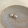 Dettaglio macro di orecchini a lobo tondi minimalisti con texture metallica spazzolata. - Argento