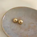 Dettaglio di orecchini a lobo rotondi dorati con finitura spazzolata opaca chic - Oro