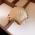 Vista detallada de un brazalete abierto de metal dorado con forma de concha y textura. - Dorado