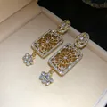 Close-up of vintage gold-tone rectangular dangle earrings with intricate floral pavé stones - Gold Brown