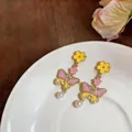 Close-up detail of vintage enamel butterfly earrings with yellow flowers and white pearl drops - Stud Earrings / Gold-Pink-Yellow