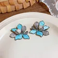Close-up of blue floral stud earrings featuring cubic zirconia and central pearls. - Flower Shape / Blue