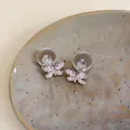 Nahaufnahme von Zirkon-Schmetterlings-Ohrsteckern mit Silbernadeln auf einem Keramikteller. - Schmetterling Design / Rosa