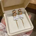 Detail of gold floral stud earrings with white resin petals and long tassels in a box - Gold