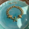 Dettaglio ravvicinato di un bracciale dorato con ciondoli stella marina e conchiglia - Oro-Blu