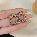 Close-up of oval hollow stud earrings featuring vibrant multi-colored baguette zircon stones. - Iridescent Gold