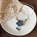 Close-up of a handcrafted blue crochet flower necklace with wooden and ceramic beads - Blue