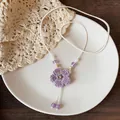 Detailed shot of a woven purple flower necklace with wood beads on a white plate - Purple