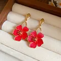 Detailed close-up view of vintage red enamel flower drop earrings in a beige jewelry box - Red