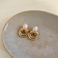 Dettaglio ravvicinato di orecchini di perle dorati stile vintage su piatto ceramico - Oro-Bianco