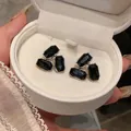 Gros plan d'élégantes boucles d'oreilles en pierres noires dans un écrin blanc. - Tige en Acier-Noir-Rectangulaire