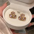 Gros plan de boucles d'oreilles dorées avec trois cristaux roses étincelants en boîte - Tige en Acier-Rose-Ovale