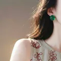 Vista macro detallada de pendientes redondos de resina verde lucidos por una modelo femenina - Verde