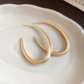 Primo piano di eleganti orecchini a cerchio ovali in oro liscio su vassoio bianco - Oro